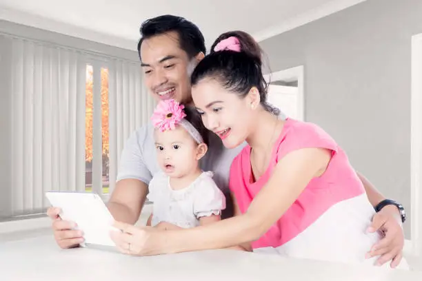 Picture of a happy Asian family using a digital tablet while sitting in the living room