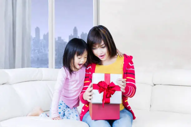 Portrait of young mother and child feel surprised while open a gift box on the sofa