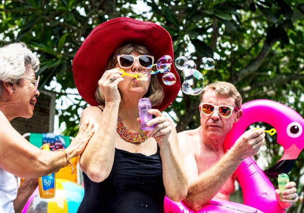 Group of diverse senior adults sitting at poolside blowing soap bubbles
