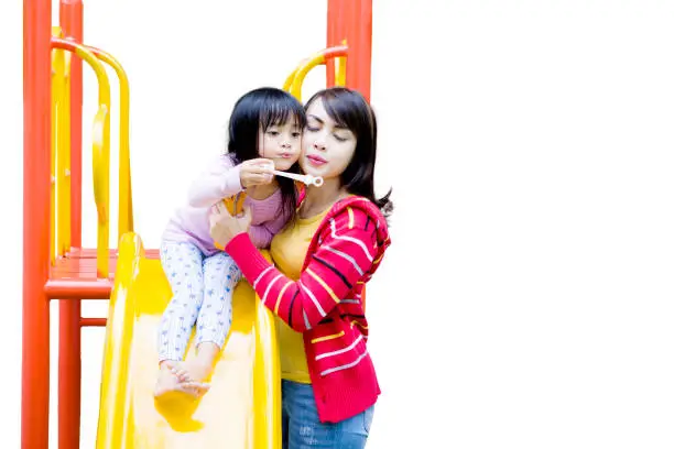 Young mother and her daughter blowing soap bubbles together in the playground, isolated on white background
