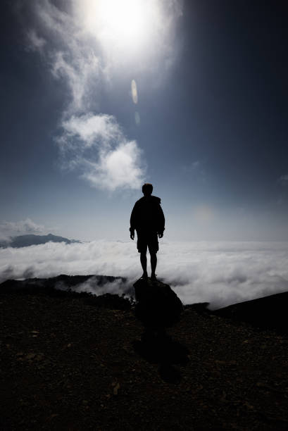 istock Man silhouette stay on rock peak with clouds below , bright sun and deep blue sky. 861143736