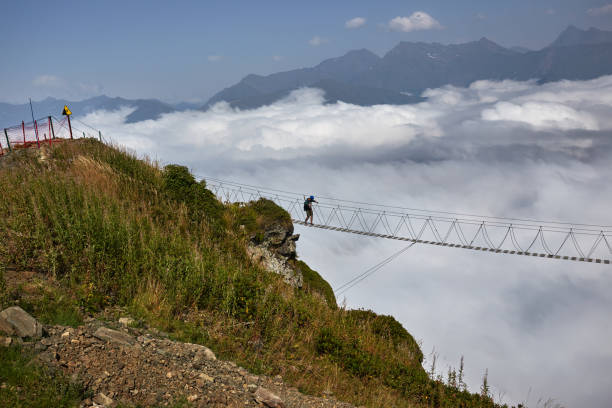 istock Man walking on suspension bridge and looking at cloudy mountains below. 861145320