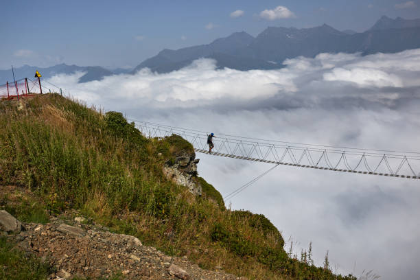 istock Man walking on suspension bridge and looking at cloudy mountains below. 861145372