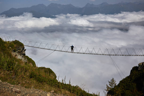istock Man walking on suspension bridge and looking at cloudy mountains below. 861145428