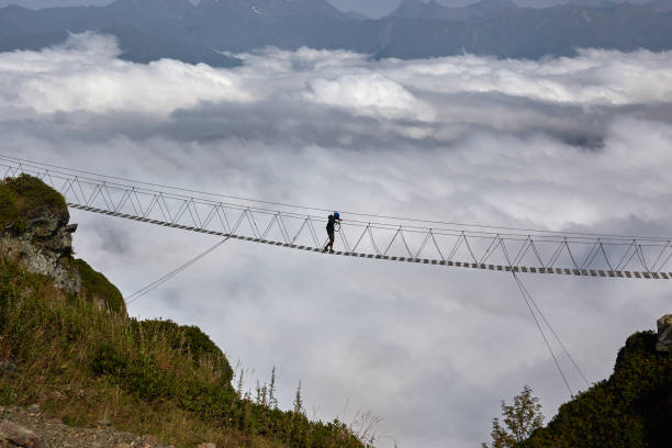 istock Man walking on suspension bridge and looking at cloudy mountains below. 861145504