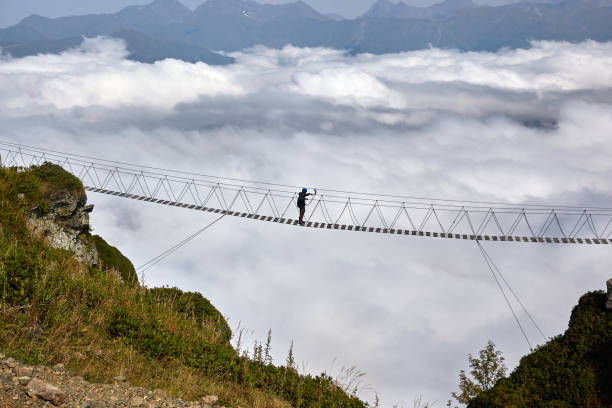 istock Man walking on suspension bridge and looking at cloudy mountains below. 861145542