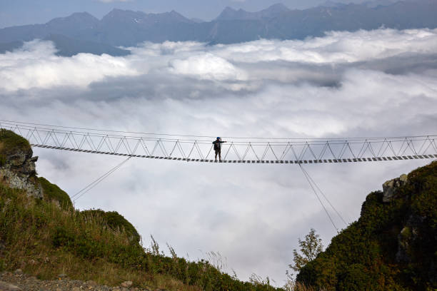 istock Man walking on suspension bridge and looking at cloudy mountains below. 861145556