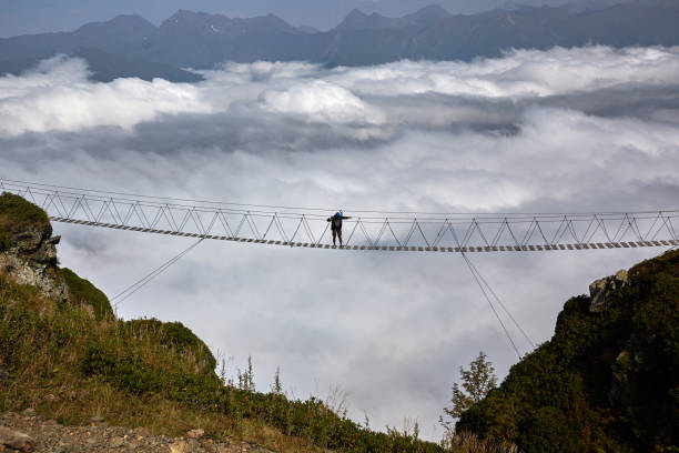 istock Man walking on suspension bridge and looking at cloudy mountains below. 861145606