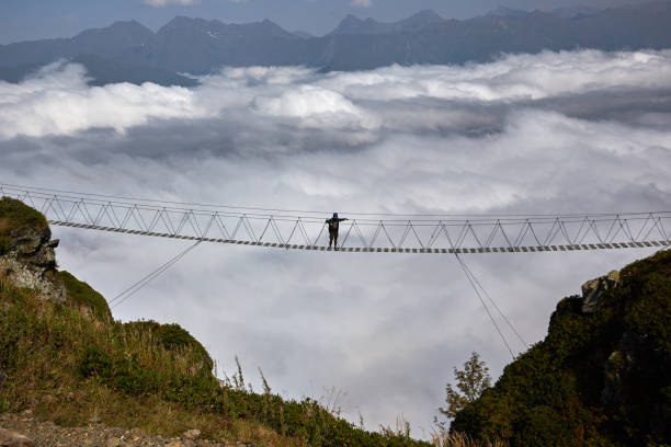 istock Man walking on suspension bridge and looking at cloudy mountains below. 861145650