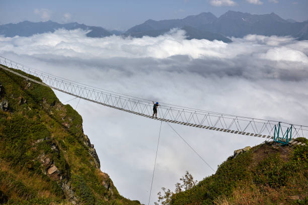 istock Man walking on suspension bridge and looking at cloudy mountains below. 861145724