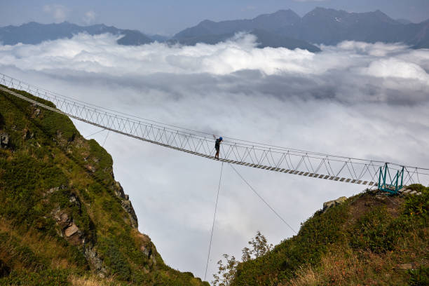 istock Man walking on suspension bridge and looking at cloudy mountains below. 861145782
