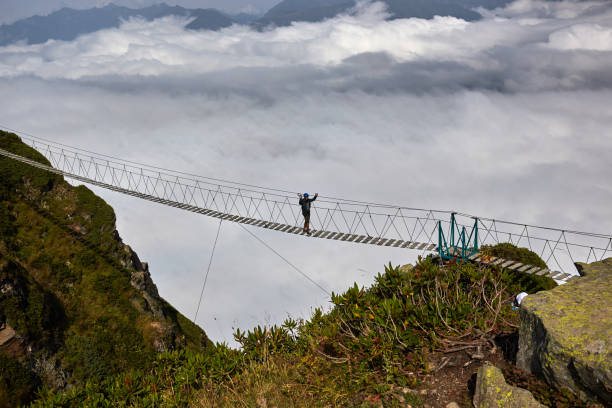istock Man walking on suspension bridge and looking at cloudy mountains below. 861146194