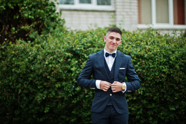 Portrait of a fashionable and stylish high school graduate in elegant tuxedo posing outdoor with bushes on the background. Portrait of a fashionable and stylish high school graduate in elegant tuxedo posing outdoor with bushes on the background. prom fashion stock pictures, royalty-free photos & images