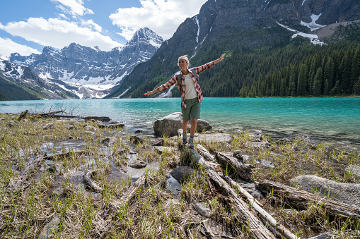 Young woman balances on a tree log above the lake. Beautiful pine tree forest and lake landscape. Shot in Banff national park, Canada.