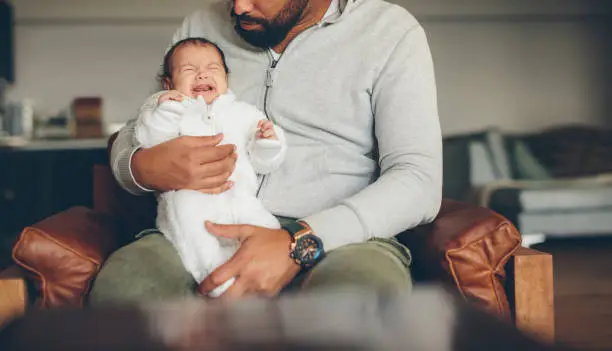 Photo of Newborn baby boy crying on his father's lap