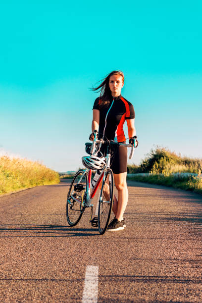 Portrait of a female athlete with cool attitude standing next to her racing bicycle Woman with cool attitude stands next to her racing bike on a country road. super bike stock pictures, royalty-free photos & images