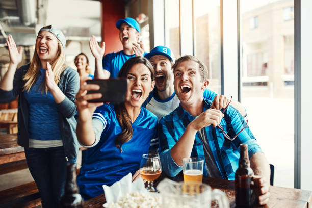 We're winning! Shot of a group of friends taking a selfie while watching a sports game at a bar friends in bar with phones stock pictures, royalty-free photos & images
