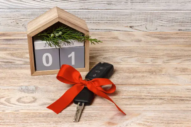 Photo of Close-up view of car keys with red bow as present and calendar on wooden background on wooden background