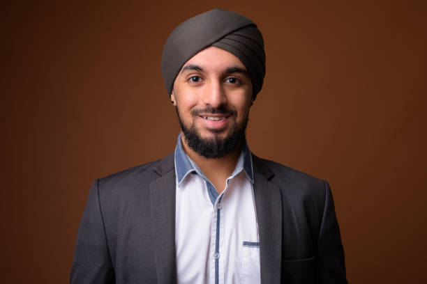 Studio shot of young bearded Indian businessman wearing suit and turban against colored background Studio shot of young bearded Indian businessman wearing suit and turban against colored background horizontal shot turban stock pictures, royalty-free photos & images