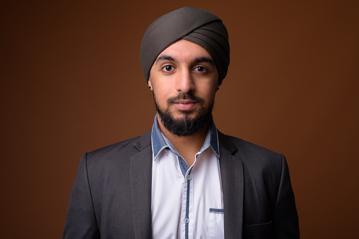 Studio shot of young bearded Indian businessman wearing suit and turban against colored background horizontal shot