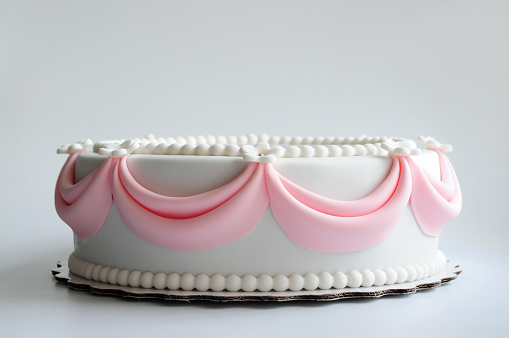 White cake with pink elements made from pastry mastic on a white background. Sugar flowers, marzipan flowers and mastic, beautiful decor for decorating cakes. For a menu or a confectionery catalog.
