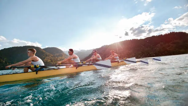 Photo of Four male athletes rowing across lake in late afternoon