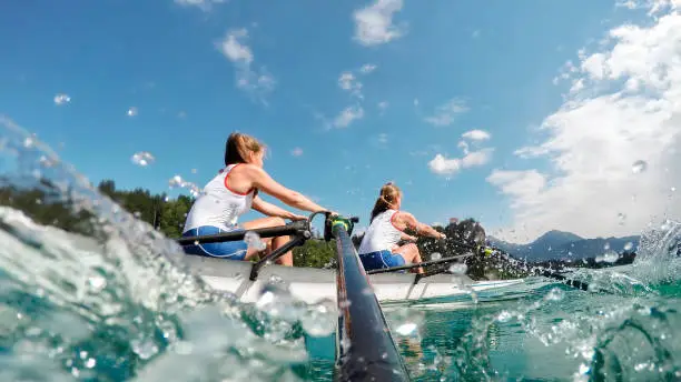 Two female rowers rowing across lake in late afternoon.