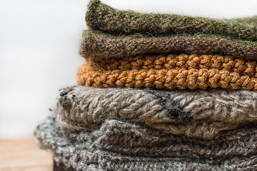 Stack of Handmade Warm Knitted Socks Scarfs Mittens From Rough Wool Yarn Brown Beige Grey on Wood Table. Close up. Winter Autumn Eco Fashion Kinfolk Style. Natural Materials