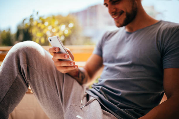 happy young man relaxing on balcony texting on mobile phone - hipster people surfing the net internet imagens e fotografias de stock