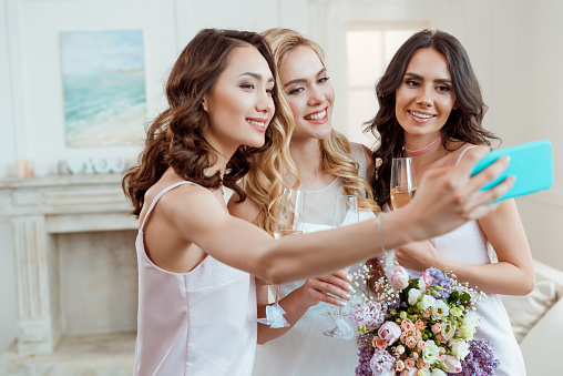 beautiful bride with bridesmaids taking selfie before ceremony