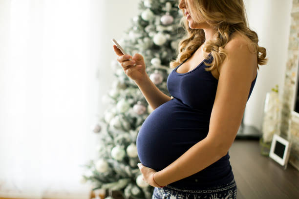 femme enceinte utilise un téléphone cellulaire avec un arbre de noël ou de nouvel an en arrière-plan - christmas tree audio photos et images de collection