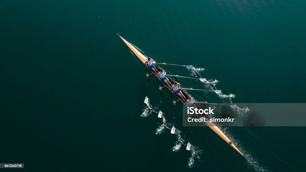 Four male athletes sculling on lake in sunshine Four male rowers sculling on lake in sunshine. Teamwork Stock Photo