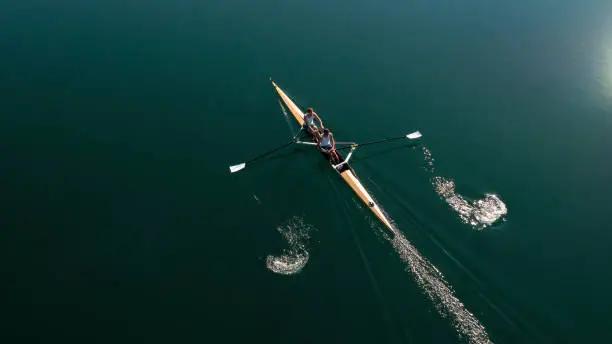 Two male rowers sculling on lake in sunshine.