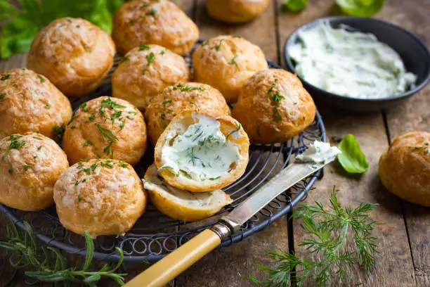 Gougeres with herb cream cheese. Traditional french cheese choux buns. wooden background.