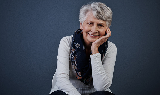 Studio shot of a cheerful elderly woman sitting down and looking straight into the camera while smiling