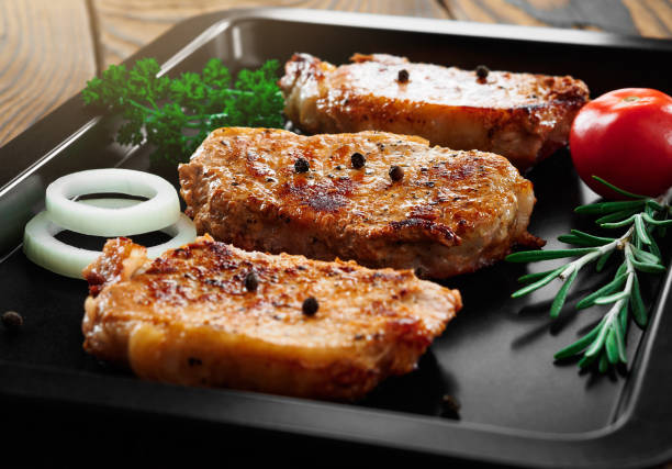 istock Baked pork steaks on a black baking sheet on wooden background 861295574
