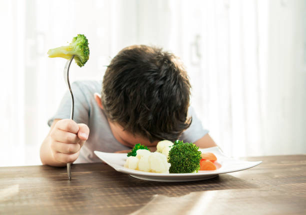 çocuk sebze yemek zorunda ile çok memnun değil. - fury stok fotoğraflar ve resimler