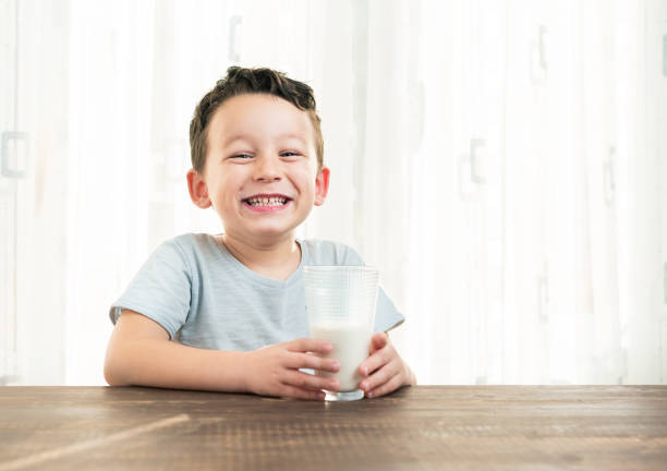Cute little Asian boy drinking a glass of milk against white background.
