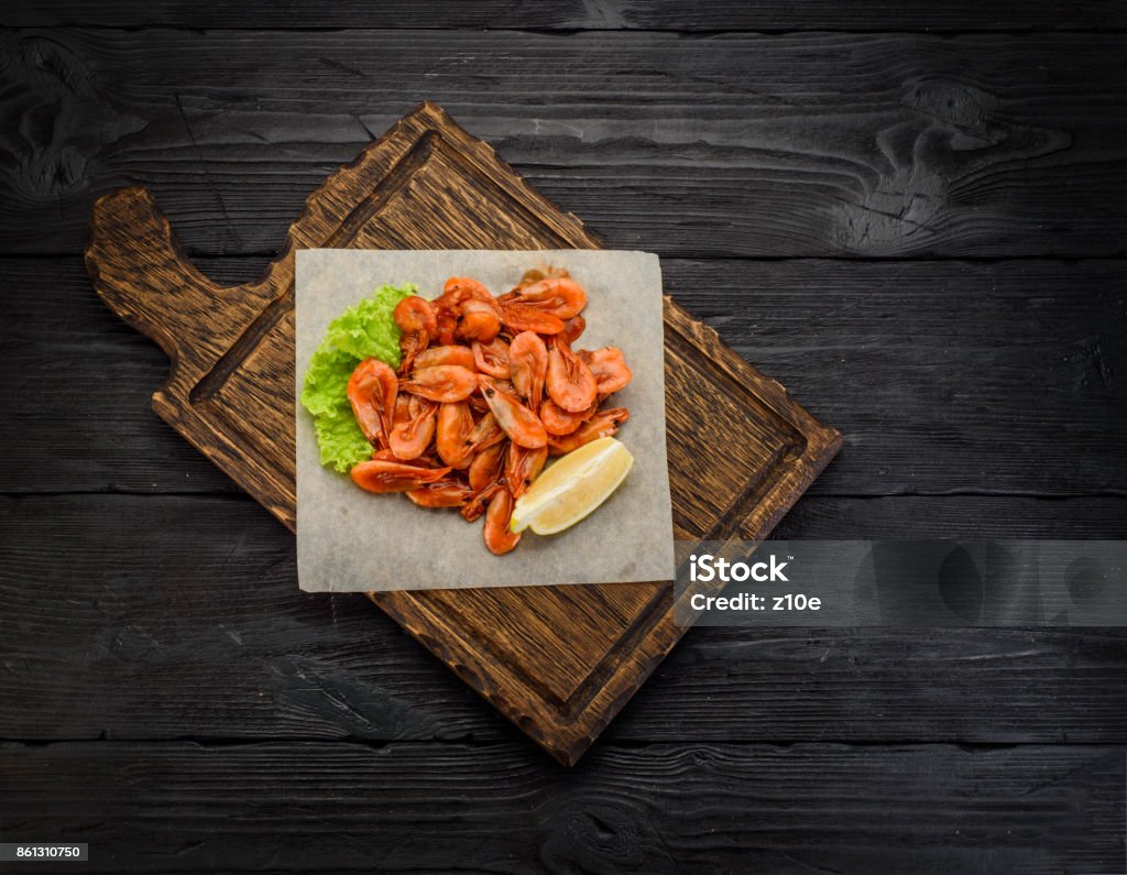 Grilled shrimps on a board and beer mug. Wooden background. Grilled shrimps on a board over dark wooden background Above Stock Photo