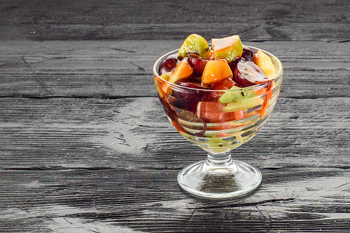 Glass of healthy fresh fruit salad on wooden background.