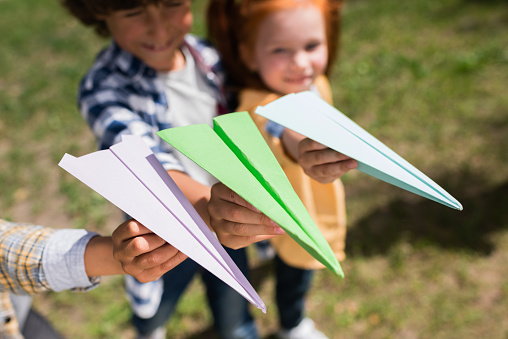 close-up view of cute little children holding paper planes in park