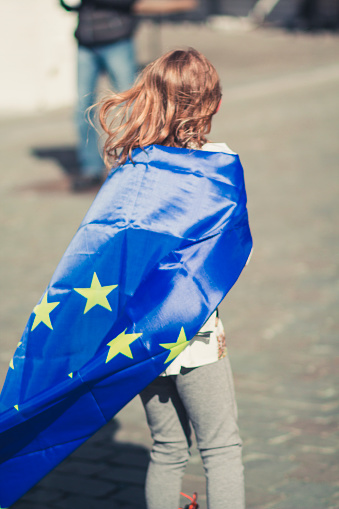 A blonde 10 year old girl sporting a european flag draped over her shoulders