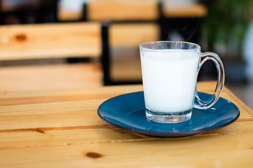 Homemade hot fresh milk in clear glass with blue saucer (bottom plate) serve on wooden table, for beverage background or texture - healthy diet concept.