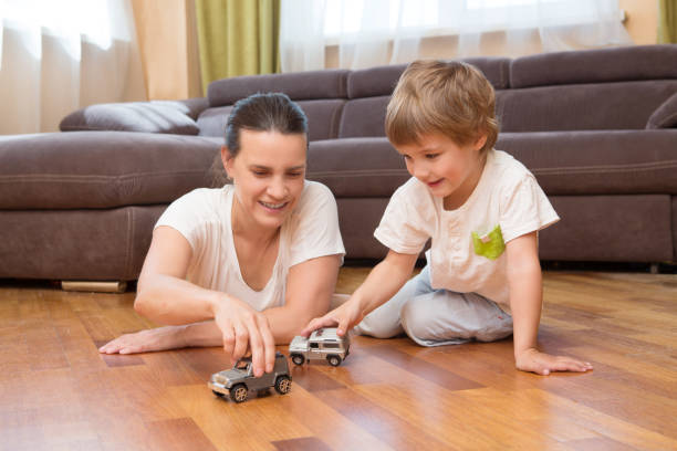Mom and her little son play car toys in their living room. The happy family spends time together at home. stock photo