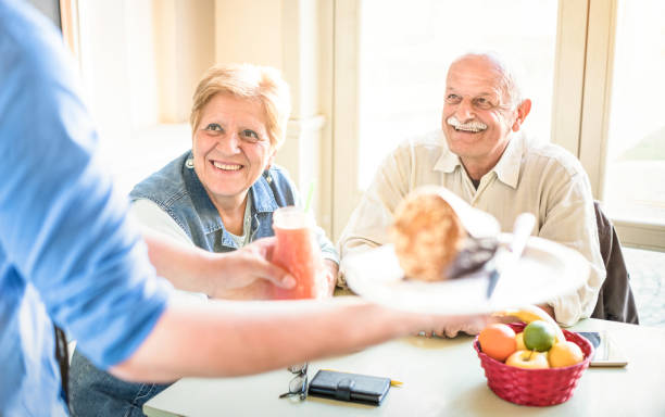 kelner serwujący starszą parę jedzącą w wegańskiej restauracji - emerytowany mężczyzna i kobieta na aktywnej zabawie w podeszłym wieku - happy retirement concept with mature people together - bright filter with focus on lady - 60s senior adult breakfast cheerful zdjęcia i obrazy z banku zdjęć