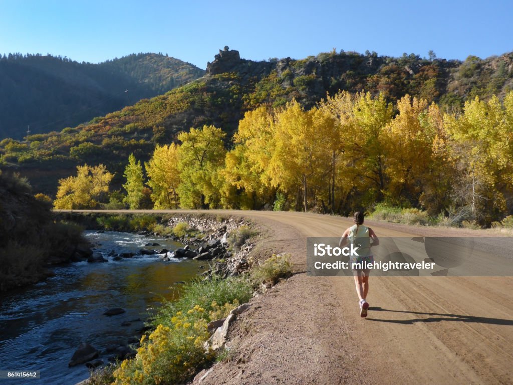Woman runs South Platte River Waterton Canyon Colorado fall colors Rocky Mountains Running along the South Platte River on a dirt road, a woman with a ponytail and shorts enjoys the fall colors and cool temperatures in the Colorado Rocky Mountains. Colorado Stock Photo