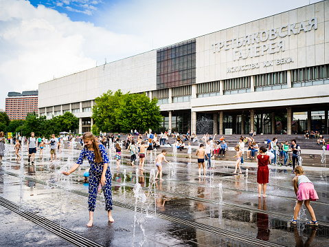 Moscow, Russia -  July 15, 2017: People enjoy summer hot day and playing with fountain's water in front of Tretyakov art gallery