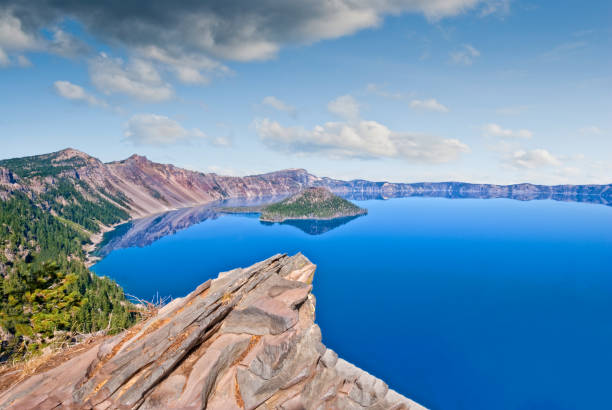 Rock Outcrop Overlooking Crater Lake Crater Lake exists in the blown-out caldera of a once mighty volcano known as Mount Mazama. This view of the lake with its calm blue water was taken from the Rim Trail in Crater Lake National Park, yyy, USA. jeff goulden crater lake national park stock pictures, royalty-free photos & images