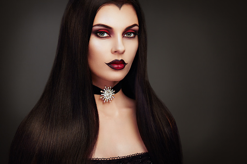 Halloween Vampire Woman portrait. Beautiful Glamour Fashion Sexy Vampire Lady with long dark Hair, beauty make up and Costume