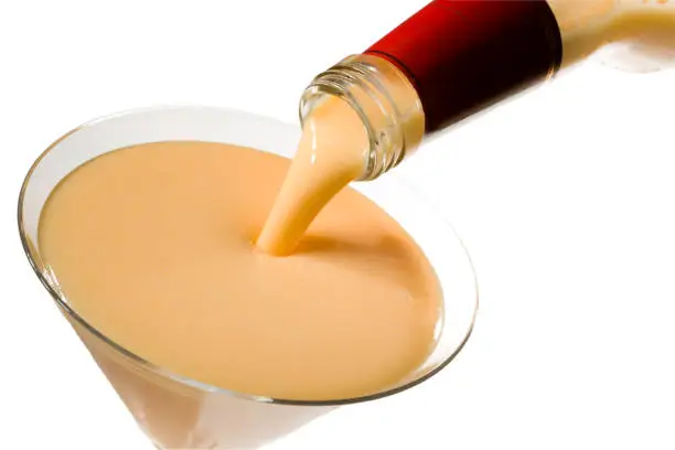 pour out egg liqueur from bottle into a glass, isolated on white, clipping path included